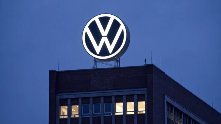 A lit up VW sign is shown on a building against a dark-blue sky.
