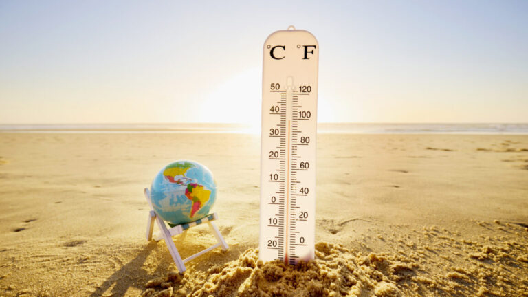 a sandy beach with a globe balanced in a beach chair next to an oversized thermometer showing high temperatures.