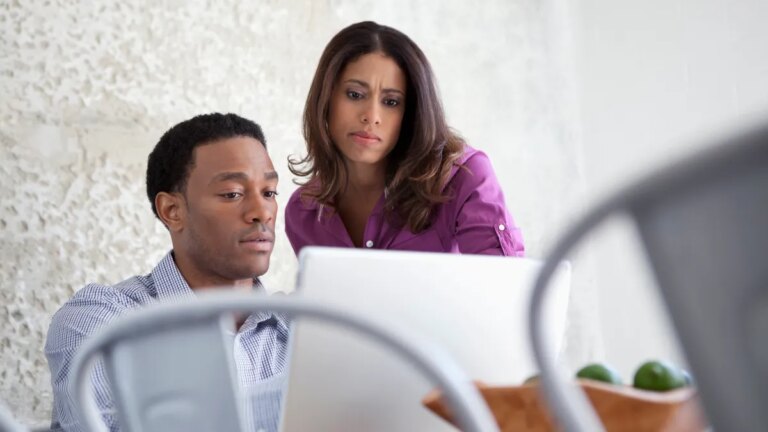 Two people look doubtfully at a laptop on a table.