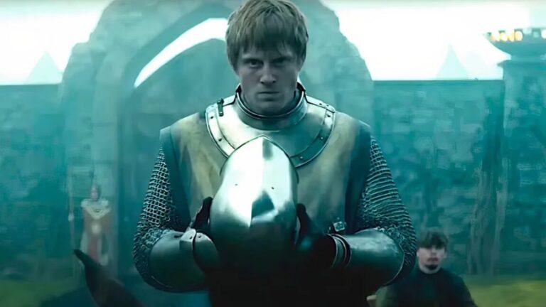 Knight in full armor staring into the camera while holding his helmet