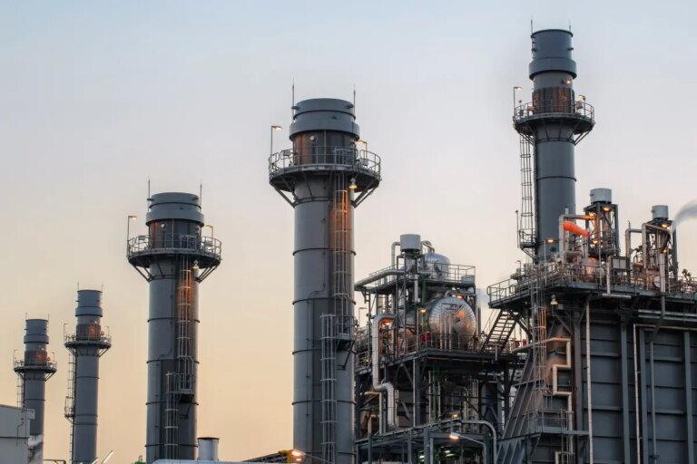 Natural gas power plant smoke stacks stand against a twilight sky.